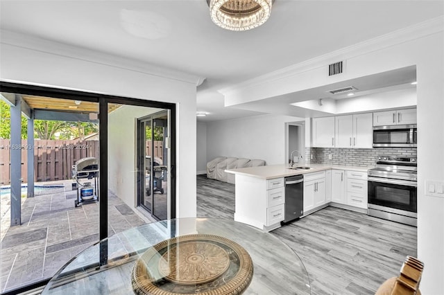 kitchen featuring appliances with stainless steel finishes, light wood-type flooring, backsplash, sink, and white cabinetry