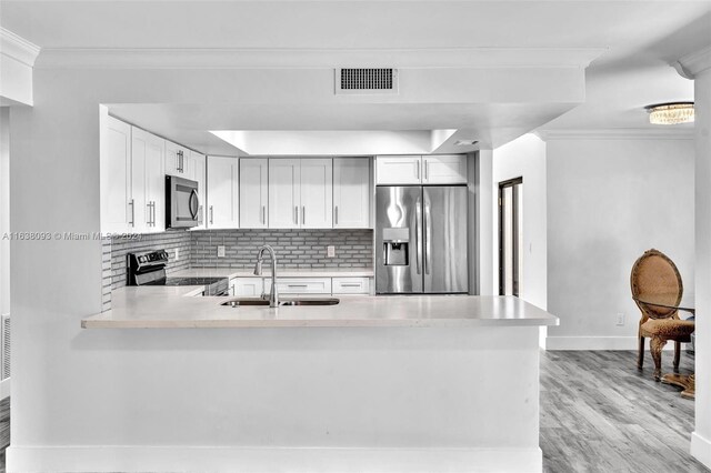 kitchen with stainless steel appliances, white cabinets, light wood-type flooring, sink, and kitchen peninsula