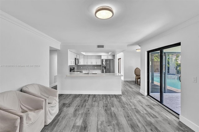 kitchen featuring stainless steel appliances, decorative backsplash, light wood-type flooring, white cabinetry, and kitchen peninsula