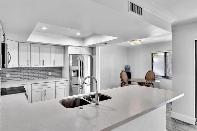 kitchen with stainless steel appliances, light hardwood / wood-style floors, sink, decorative backsplash, and kitchen peninsula