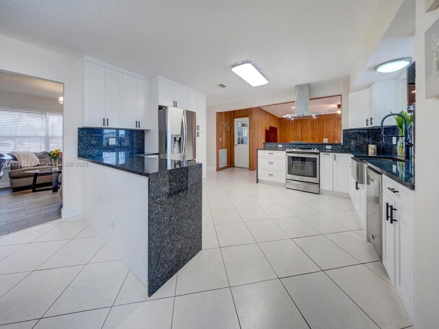 kitchen featuring kitchen peninsula, wooden walls, white cabinets, exhaust hood, and appliances with stainless steel finishes