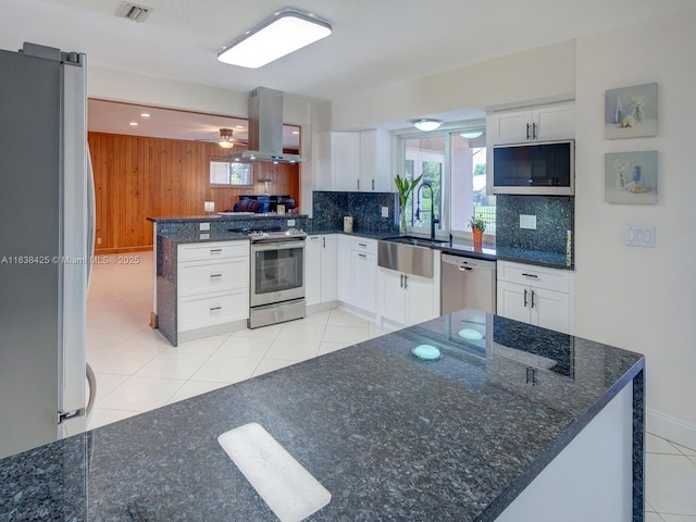 kitchen with wood walls, sink, white cabinetry, island exhaust hood, and stainless steel appliances