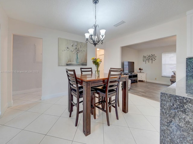 dining space with light tile patterned floors, baseboards, visible vents, a textured ceiling, and a notable chandelier