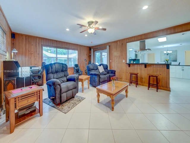 living area with ceiling fan with notable chandelier, light tile patterned floors, recessed lighting, and wooden walls