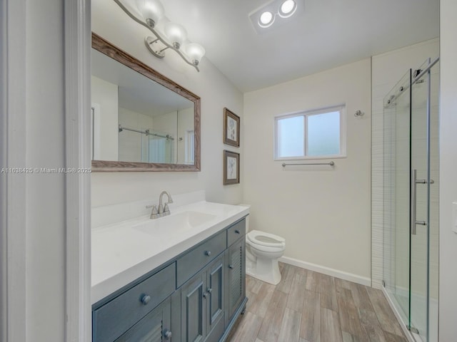 bathroom with toilet, a shower stall, vanity, wood finished floors, and baseboards