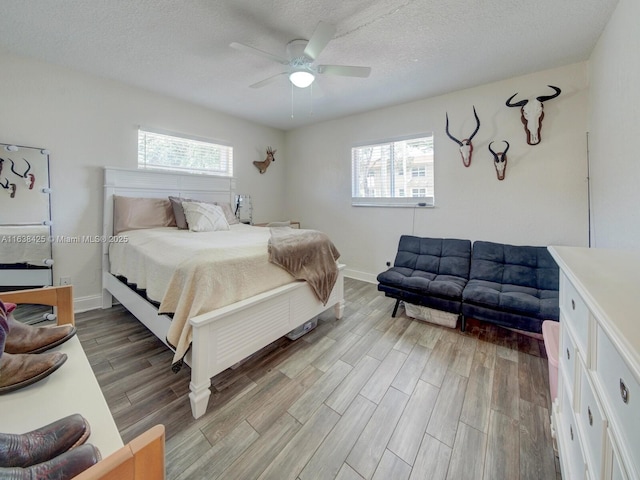 bedroom with a ceiling fan, multiple windows, a textured ceiling, and wood finished floors