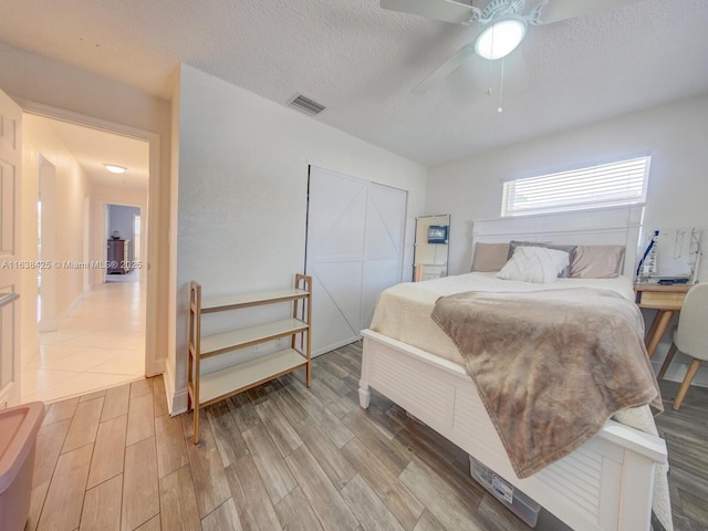 bedroom featuring light wood-style floors, a closet, visible vents, and a textured ceiling