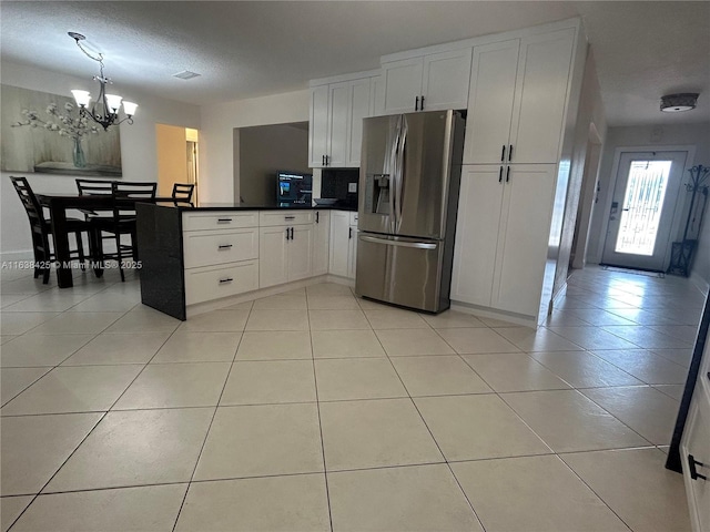 kitchen with light tile patterned floors, dark countertops, white cabinets, stainless steel fridge, and a peninsula