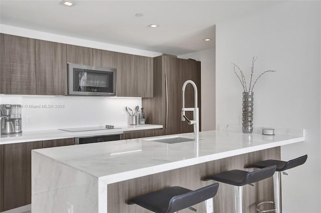 kitchen featuring kitchen peninsula, light stone countertops, black electric stovetop, sink, and a breakfast bar area