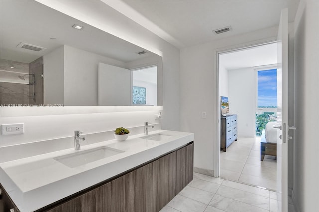 bathroom with tiled shower, dual vanity, and tile patterned flooring