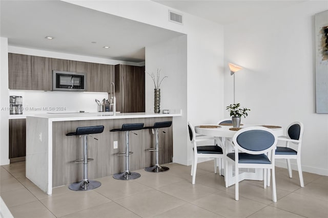 kitchen with a breakfast bar area, light tile patterned flooring, sink, and kitchen peninsula