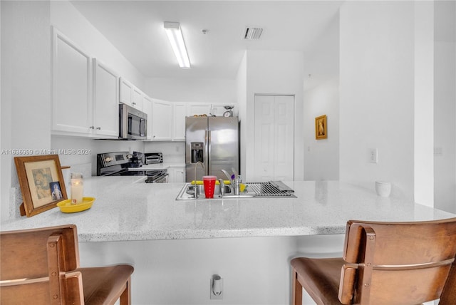 kitchen with kitchen peninsula, white cabinets, appliances with stainless steel finishes, sink, and a kitchen bar