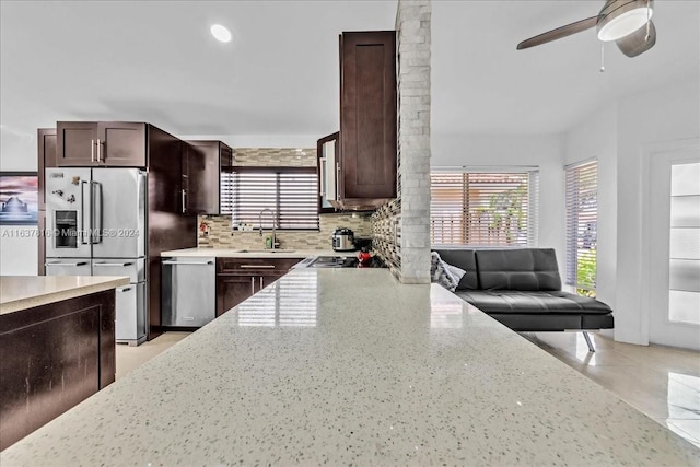 kitchen with appliances with stainless steel finishes, light stone countertops, ceiling fan, backsplash, and sink