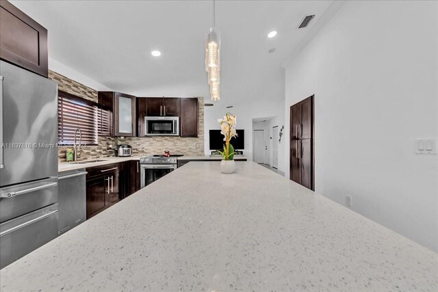 kitchen with dark brown cabinets, hanging light fixtures, premium appliances, sink, and decorative backsplash