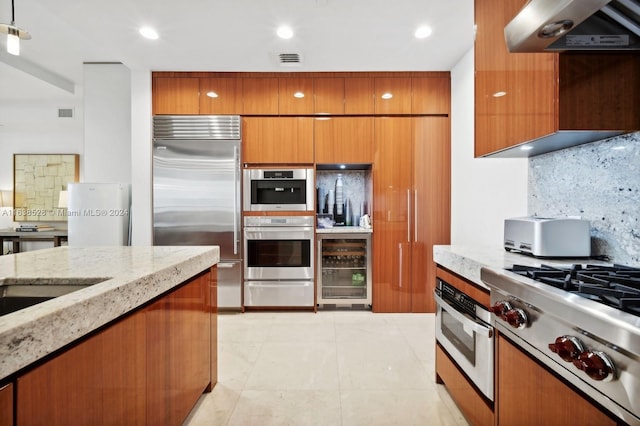 kitchen featuring decorative backsplash, appliances with stainless steel finishes, wine cooler, light stone counters, and wall chimney exhaust hood