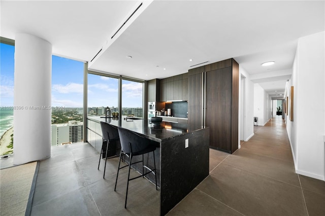 kitchen featuring a wall of windows, a water view, dark brown cabinetry, a center island with sink, and a breakfast bar