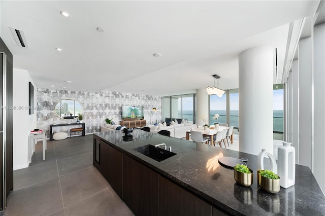 kitchen featuring dark stone countertops, hanging light fixtures, dark brown cabinets, sink, and dark tile patterned floors