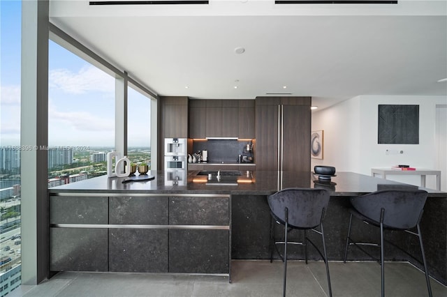 kitchen with floor to ceiling windows, dark brown cabinets, tasteful backsplash, and a kitchen bar