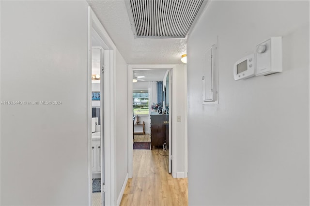 hall featuring light wood-type flooring, a textured ceiling, and electric panel