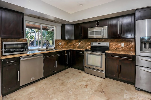 kitchen with decorative backsplash, appliances with stainless steel finishes, light stone countertops, dark brown cabinetry, and sink