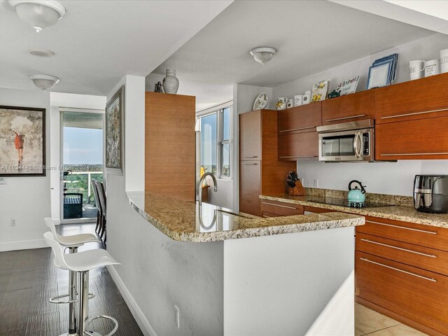 kitchen featuring light tile patterned floors, light stone countertops, a kitchen bar, black electric stovetop, and sink