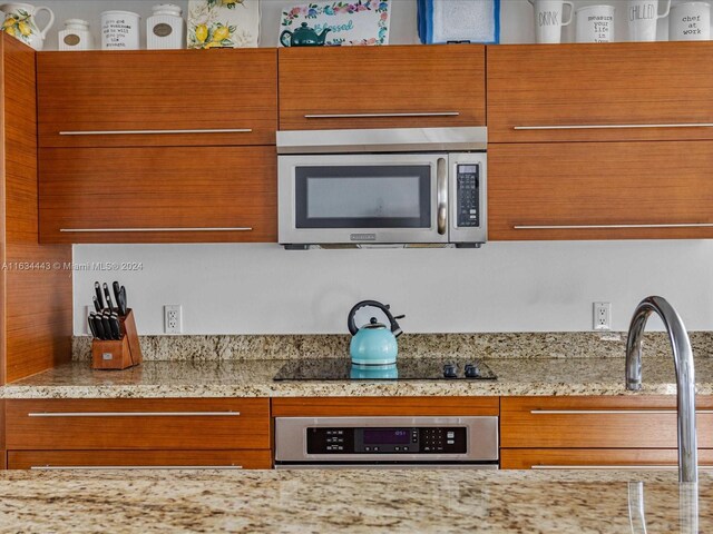 kitchen featuring light stone countertops, sink, black electric stovetop, and oven