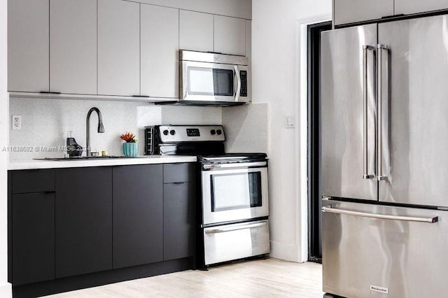 kitchen with appliances with stainless steel finishes, sink, light wood-type flooring, and tasteful backsplash