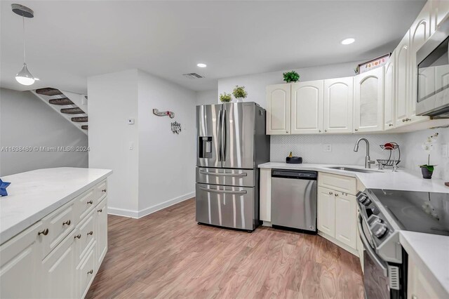 kitchen featuring pendant lighting, appliances with stainless steel finishes, light hardwood / wood-style floors, backsplash, and sink