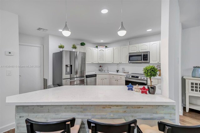 kitchen with appliances with stainless steel finishes, hardwood / wood-style floors, a kitchen bar, white cabinetry, and decorative light fixtures