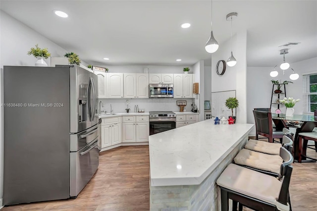 kitchen featuring appliances with stainless steel finishes, light hardwood / wood-style flooring, white cabinets, and pendant lighting