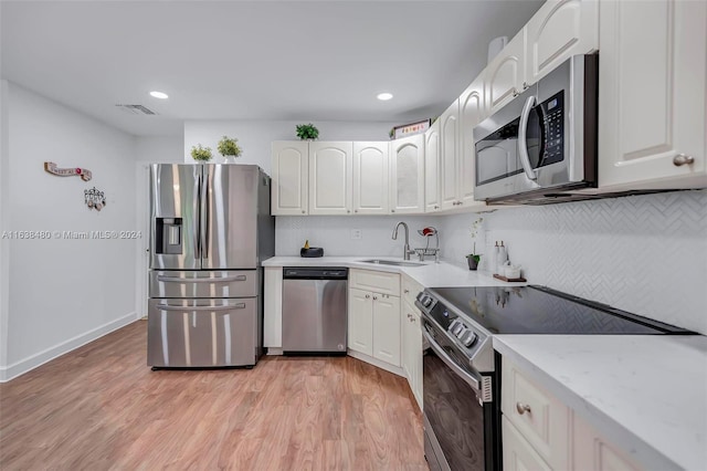 kitchen with appliances with stainless steel finishes, white cabinets, sink, and light hardwood / wood-style floors