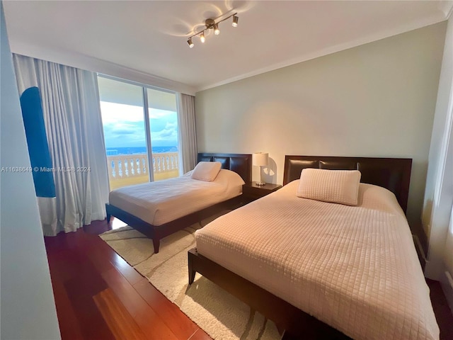 bedroom featuring hardwood / wood-style flooring, crown molding, a water view, access to exterior, and rail lighting