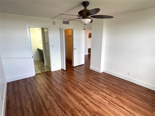 unfurnished bedroom with ceiling fan, dark wood-type flooring, a walk in closet, connected bathroom, and a closet