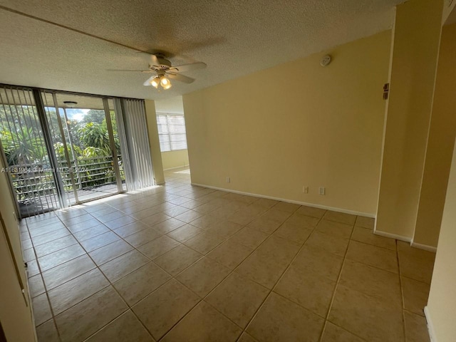 tiled empty room with ceiling fan, a wall of windows, and a textured ceiling