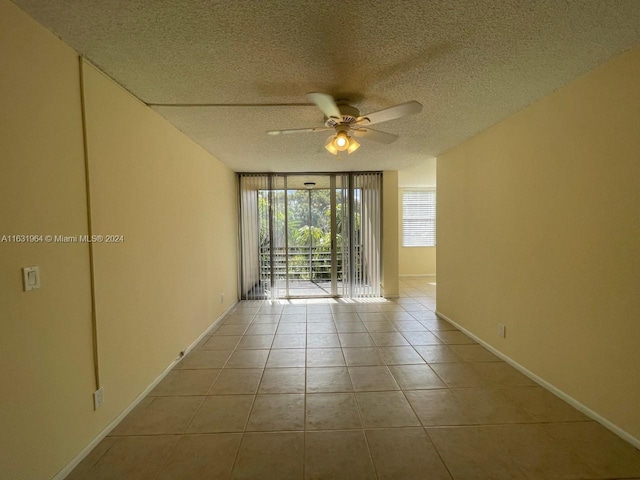 tiled spare room with ceiling fan, expansive windows, and a textured ceiling