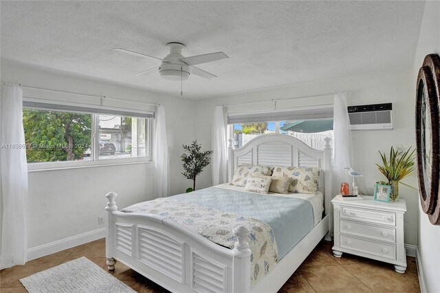 tiled bedroom with a wall mounted AC, ceiling fan, and a textured ceiling