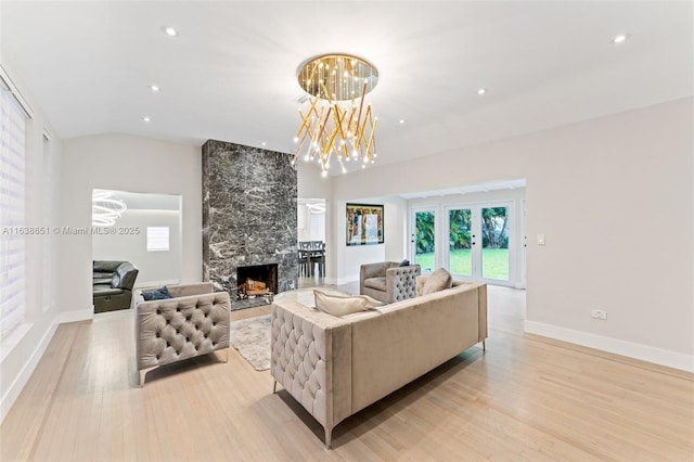 living room featuring light wood-type flooring, an inviting chandelier, a tile fireplace, and lofted ceiling