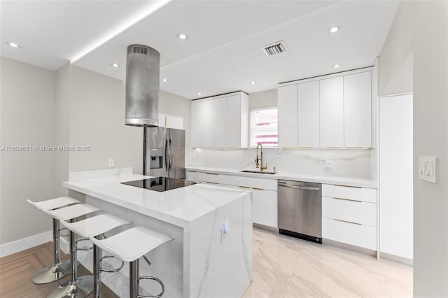 kitchen featuring sink, white cabinetry, a breakfast bar area, island range hood, and appliances with stainless steel finishes