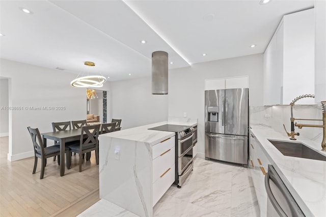 kitchen with stainless steel appliances, light stone counters, sink, white cabinetry, and decorative light fixtures