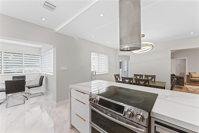 kitchen with light stone counters, range with two ovens, a healthy amount of sunlight, and white cabinetry