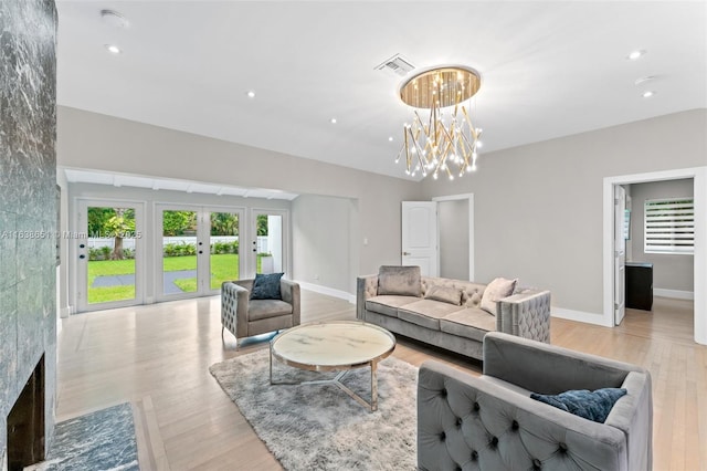 living room with a notable chandelier, light hardwood / wood-style floors, french doors, and a wealth of natural light