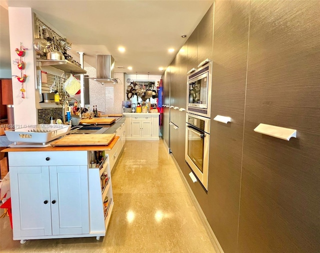 kitchen featuring kitchen peninsula, wall chimney range hood, white cabinets, and stainless steel appliances