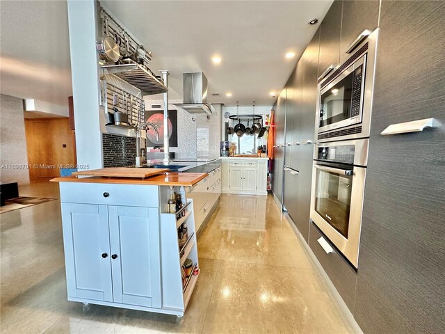 kitchen featuring wall chimney range hood, ornate columns, and appliances with stainless steel finishes