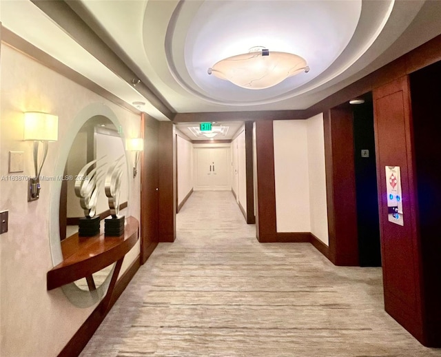 corridor with light wood-type flooring and a raised ceiling