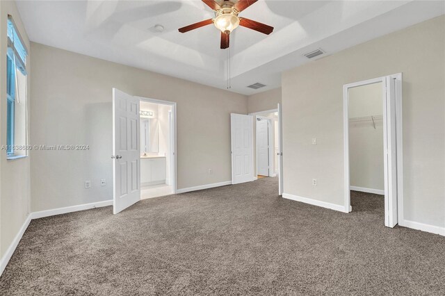 unfurnished bedroom featuring carpet flooring, ceiling fan, a spacious closet, ensuite bathroom, and a raised ceiling