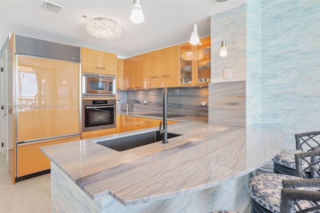 kitchen featuring visible vents, a peninsula, a sink, light brown cabinetry, and built in appliances