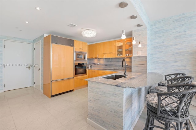 kitchen with glass insert cabinets, light stone countertops, built in appliances, a peninsula, and a sink