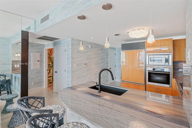 kitchen featuring built in appliances, tile walls, light tile patterned floors, sink, and decorative light fixtures