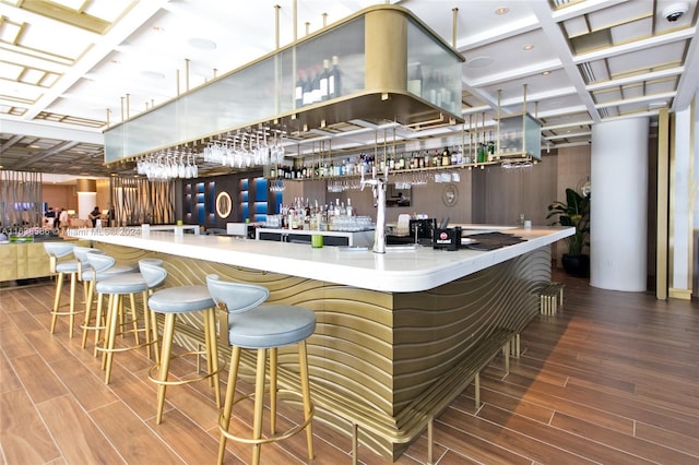 bar featuring coffered ceiling, wood tiled floor, and a community bar