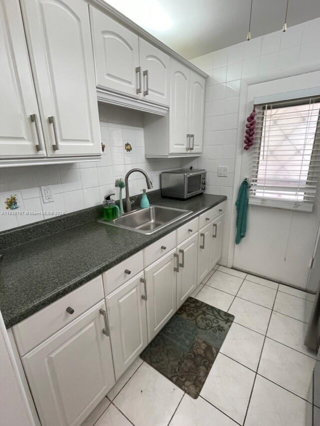 kitchen featuring decorative backsplash, light tile patterned flooring, white cabinets, and sink